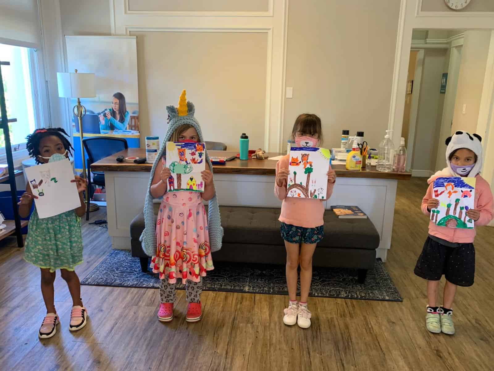 Four KidzToPros summer campers hold up paintings while wearing masks.