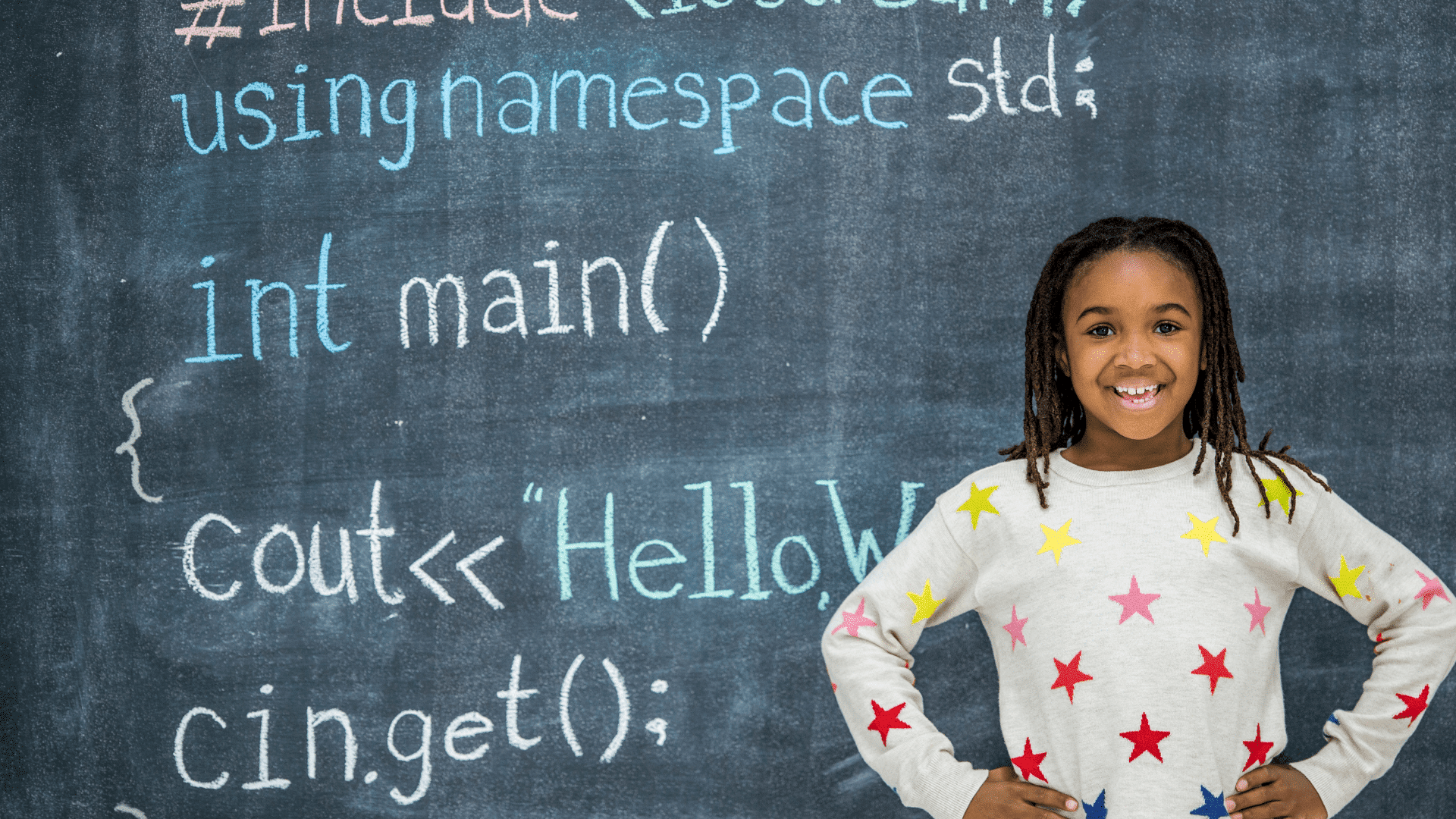 A girl stands in front of a chalkboard with code written on it